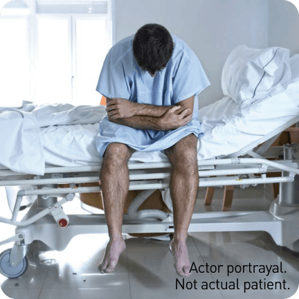 Actor portrayal of FCS patient hunched over on hospital bed with abdominal pain